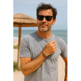 Homme d’une quarantaine d’années en t-shirt gris portant le bracelet rouge Gambier à trois perles de Tahiti, en bord de mer.