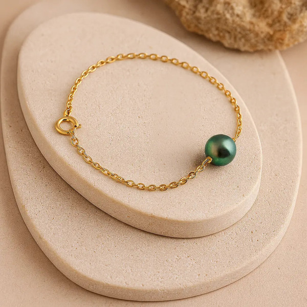 Bracelet en or jaune 18 carats avec perle de Tahiti ronde peacock – mise en scène sur présentoir en pierre beige