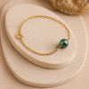 Bracelet en or jaune 18 carats avec perle de Tahiti ronde peacock – mise en scène sur présentoir en pierre beige