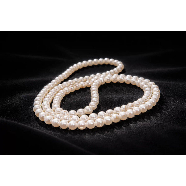 Sautoir de perles d’eau douce Sophia posé sur fond sombre, perles blanches brillantes