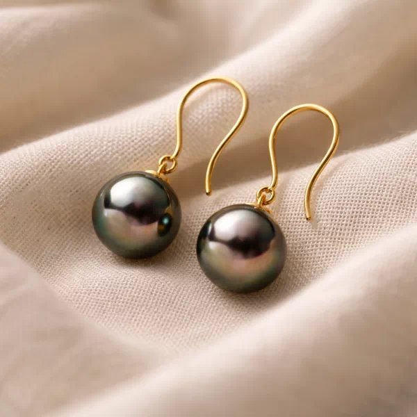 18k yellow gold earrings with 8 mm round Tahitian pearls resting on soft light linen fabric