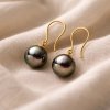 18k yellow gold earrings with 8 mm round Tahitian pearls resting on soft light linen fabric